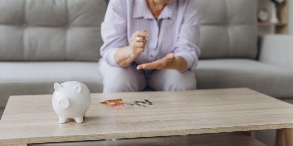 smiling senior woman putting coins into piggy bank at home
