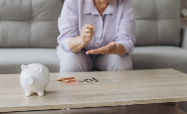 smiling senior woman putting coins into piggy bank at home