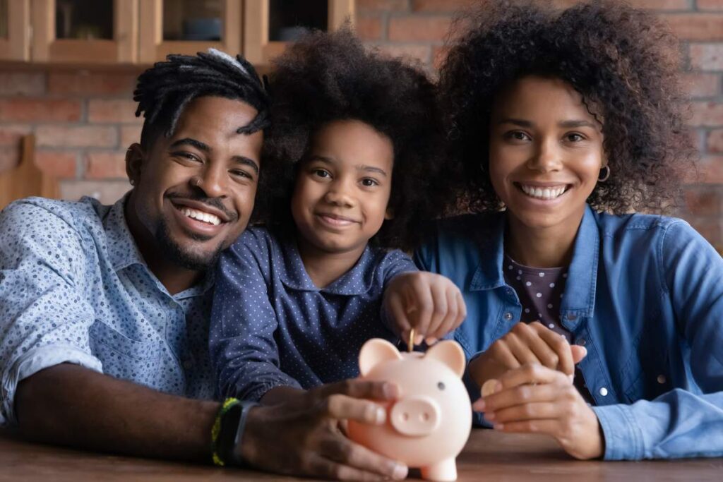 Portrait of happy young African American family with teen daughter put coin save money in piggybank. Smiling economical ethnic parents with child feel provident make financial investment for future.