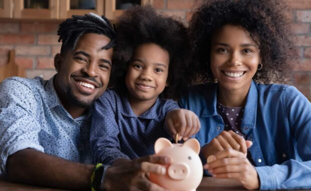 Portrait of happy young African American family with teen daughter put coin save money in piggybank. Smiling economical ethnic parents with child feel provident make financial investment for future.