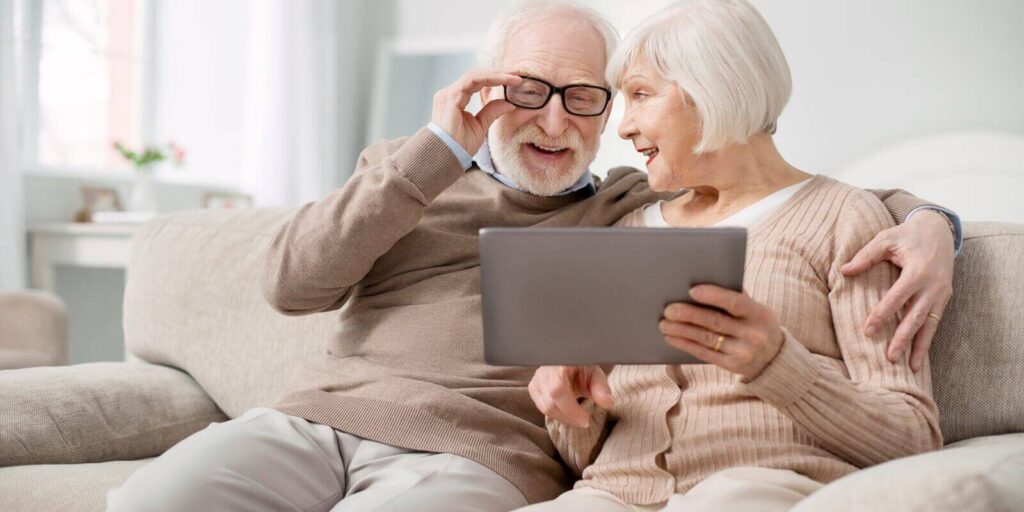 delighted aged man fixing his glasses while looking at the tablet screen