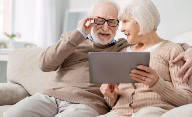 delighted aged man fixing his glasses while looking at the tablet screen