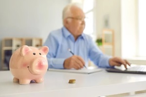 piggy bank standing on desk with blurred retired man using laptop and doing accounting in background